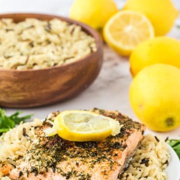 a plate topped with rice pilaf and a piece of salmon on the counter in front of a bowl of rice and a pile of lemons