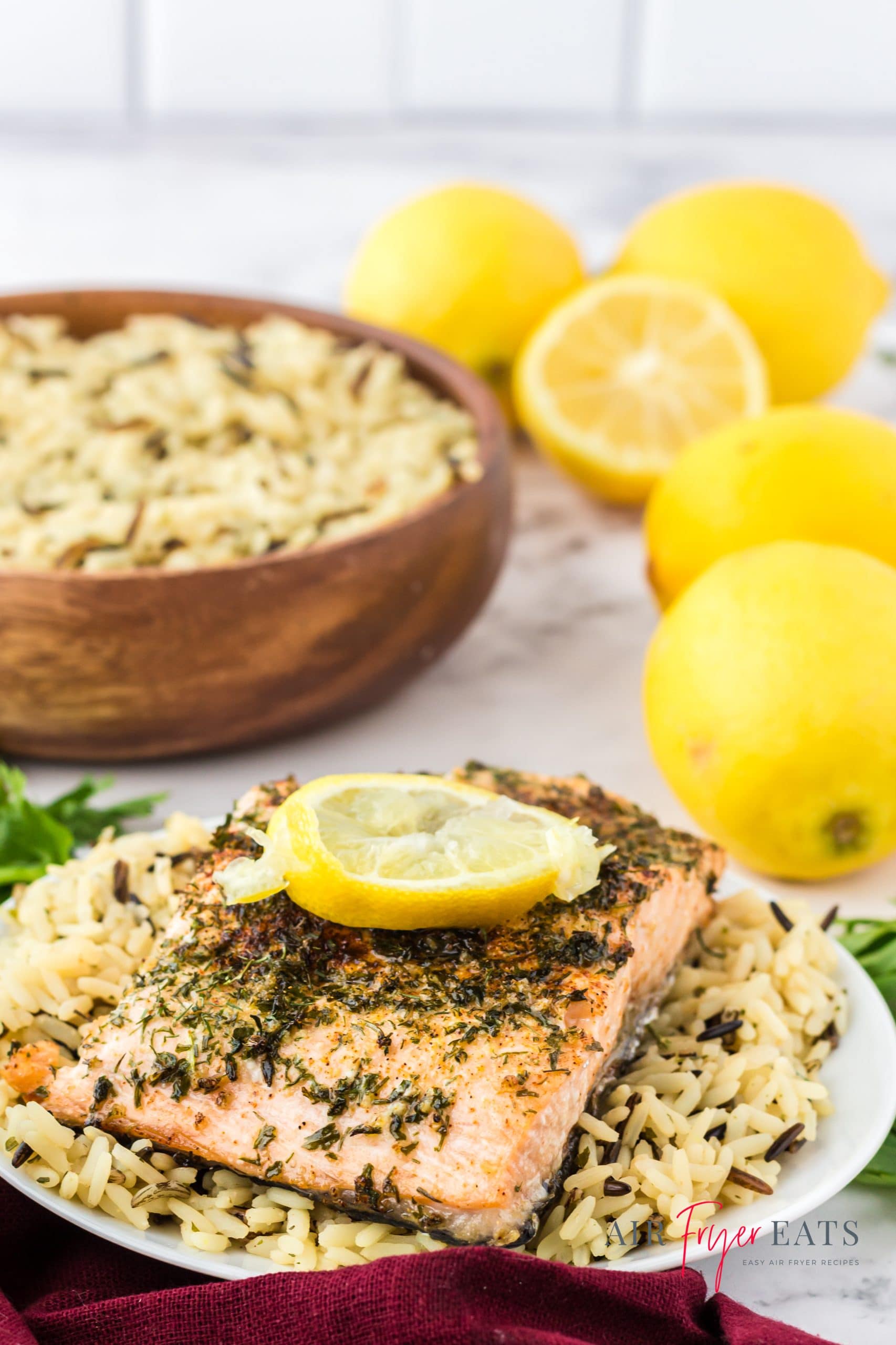 a plate topped with rice pilaf and a piece of salmon on the counter in front of a bowl of rice and a pile of lemons