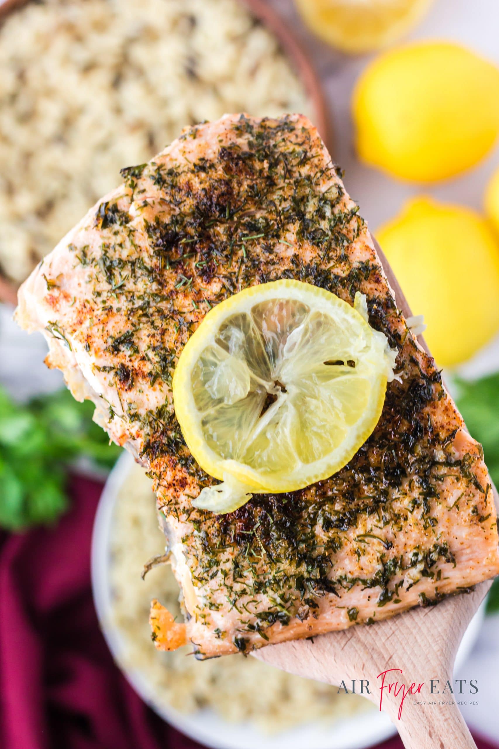 a salmon fillet topped with herbs and a lemon slice, held up with a spatula. 