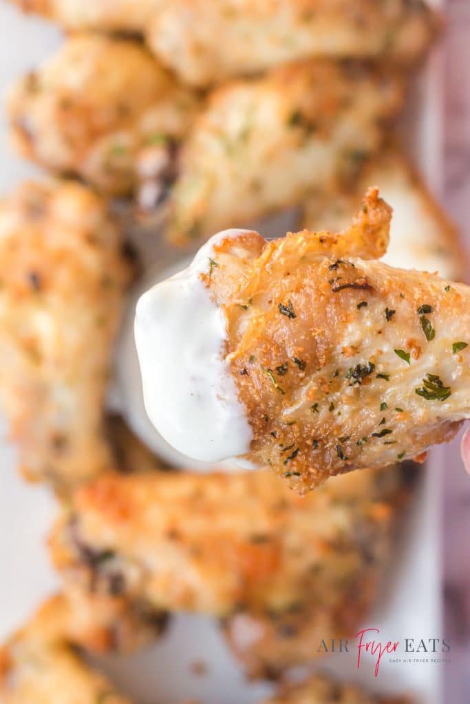 one drumette wing dipped in ranch dressing, held above a platter of wings