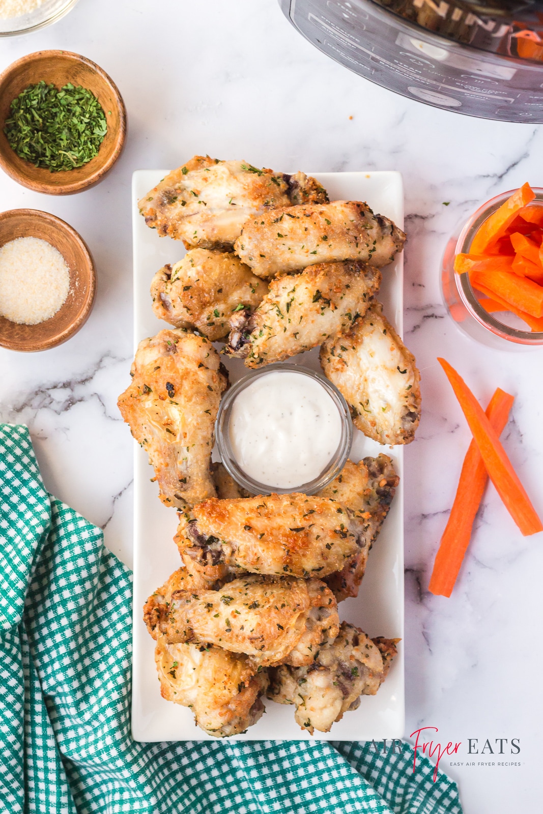 a rectangular platter of chicken wings with a cup of ranch in the center and a side of carrot sticks