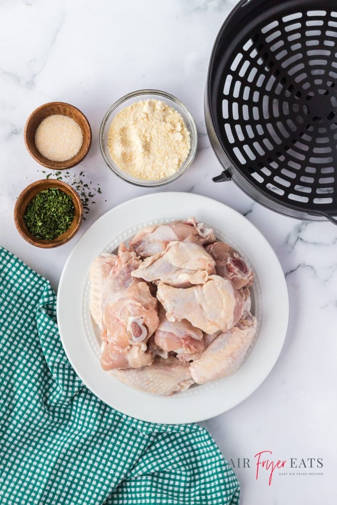 Ingredients needed to make chicken wings in ninja foodi air fryer, set out on a marble counter with a green kitchen towel and the ninja basket.