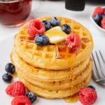a stack of frozen waffles that were cooked in the air fryer, topped with syrup, fresh berries, and a pat of butter.