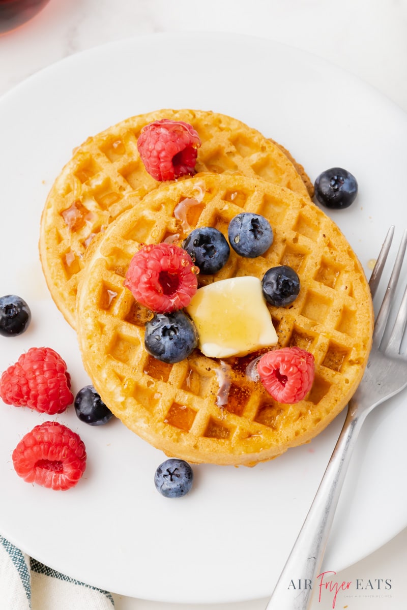 two frozen waffles on a plate topped with butter, syrup, and fresh raspberries and blueberries