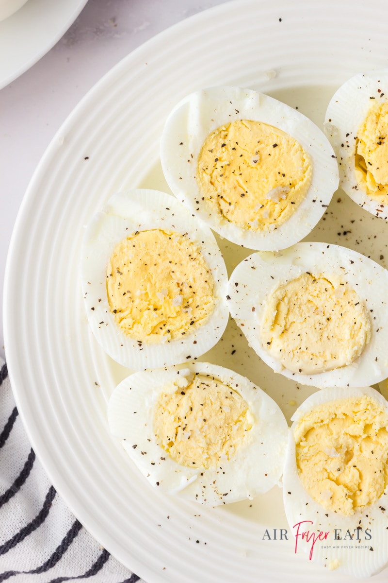 a white plate filled with halved and peeled hard boiled eggs topped with black pepper