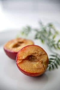 Vertical photo of an air fried plum sliced into two halves on a plate with green leaves for decoration