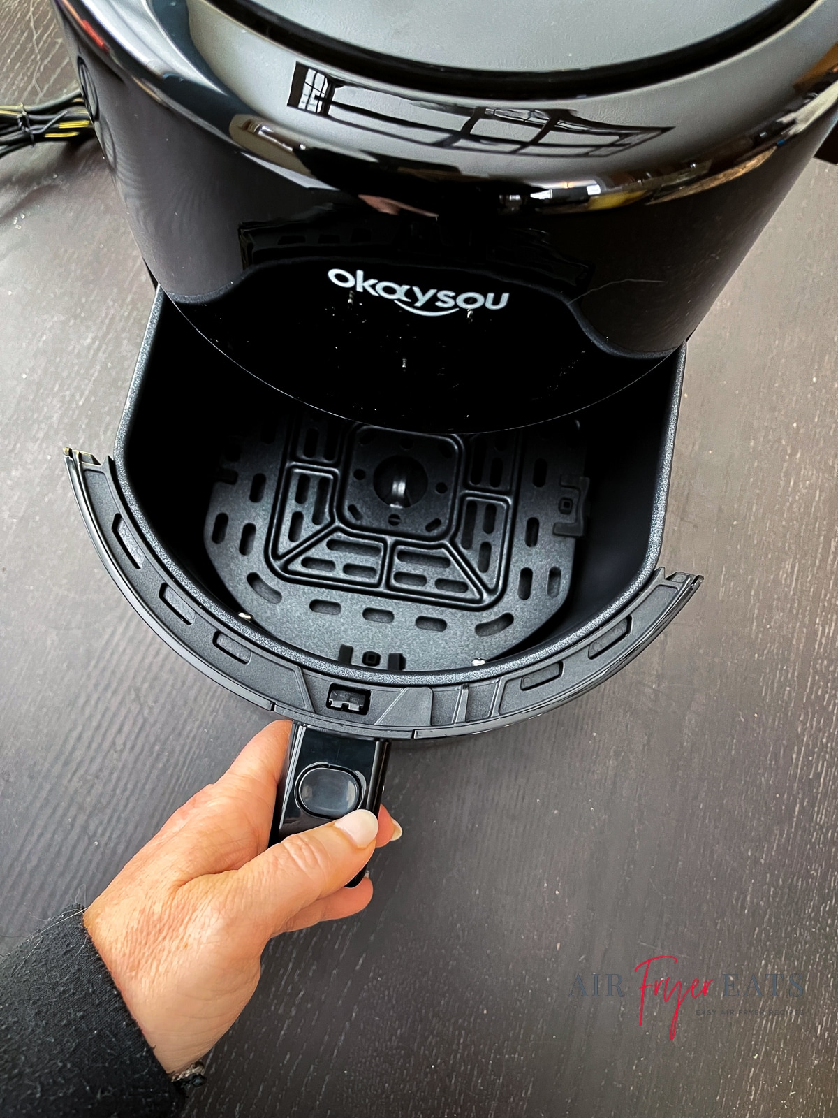 black okaysou air fryer on black table with hand pulling out basket