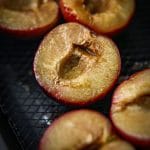 Close up photo of air fried plum halves sat in a black air fryer basket.