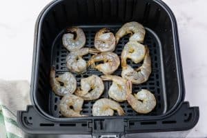 Uncooked shrimp in a black air fryer basket. Top down view