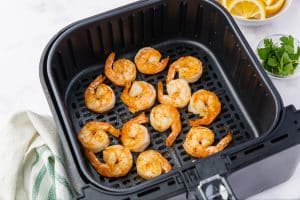 Cooked shrimp with an orange color in a black air fryer basket, the view is top down.