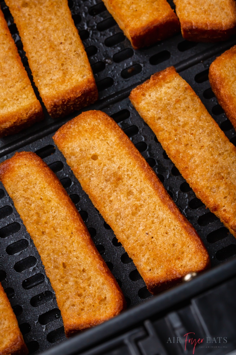 cooked frozen french toast sticks lined up in a square air fryer basket. 