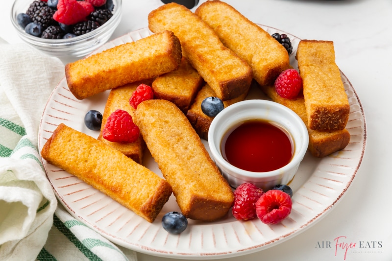a plate of french toast sticks with berries and syrup