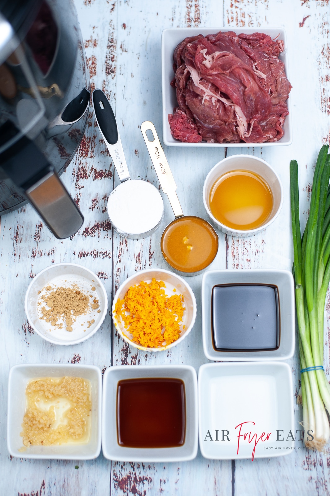 Overhead shot of ingredients for air fryer orange beef. Cornstarch, beef, orange juice and zest, molasses, rice vinegar, soy sauce, minced garlic, ginger powder, sesame oil and green onions.