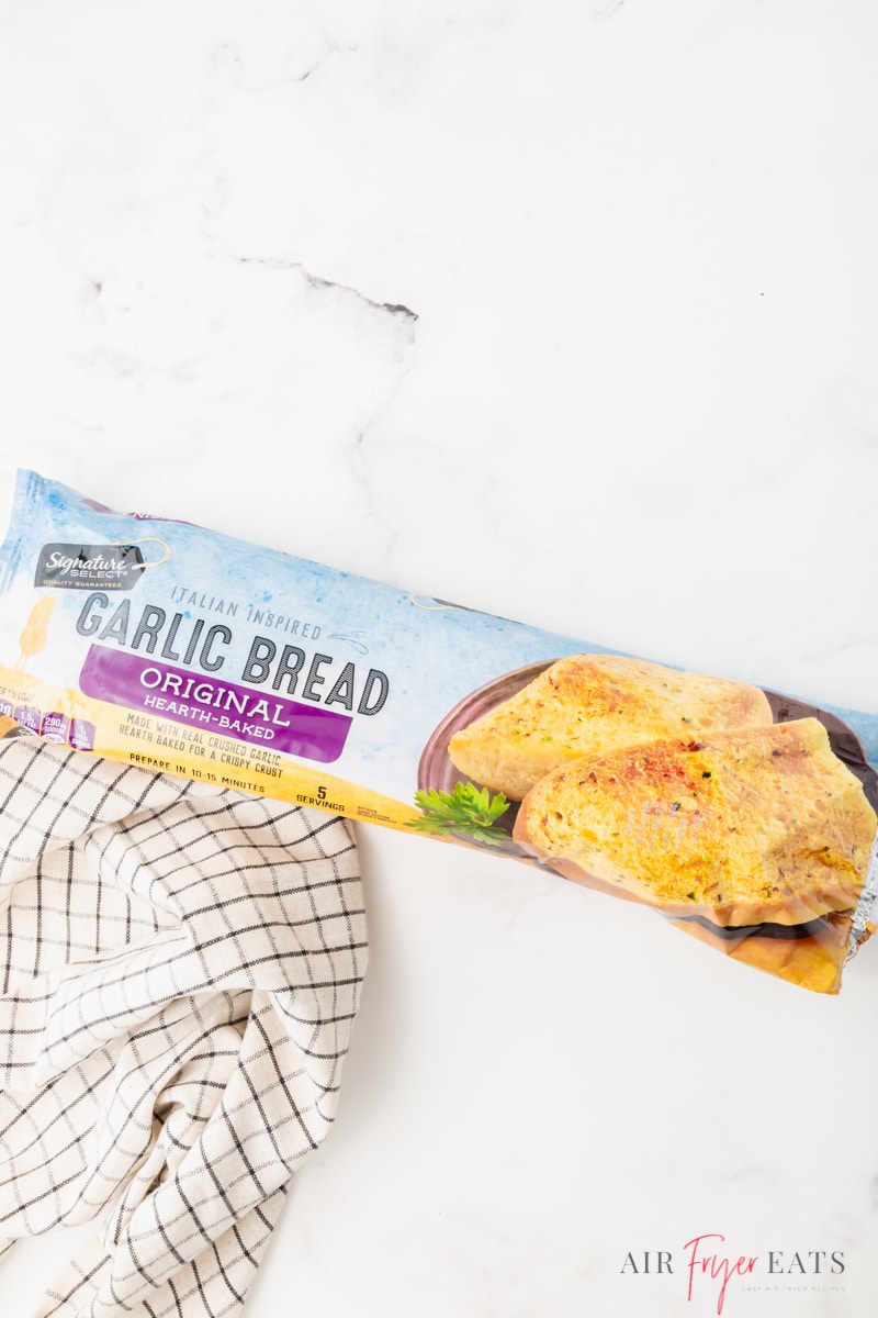 a packaged frozen garlic bread loaf on a marble countertop next to a checked kitchen towel