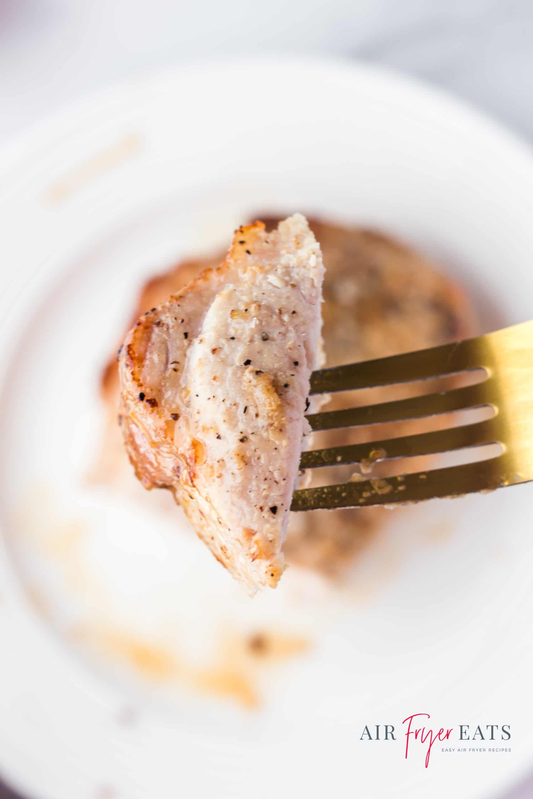 a gold fork holding a bite of an air fried pork chop above a plate with a pork chop on it.