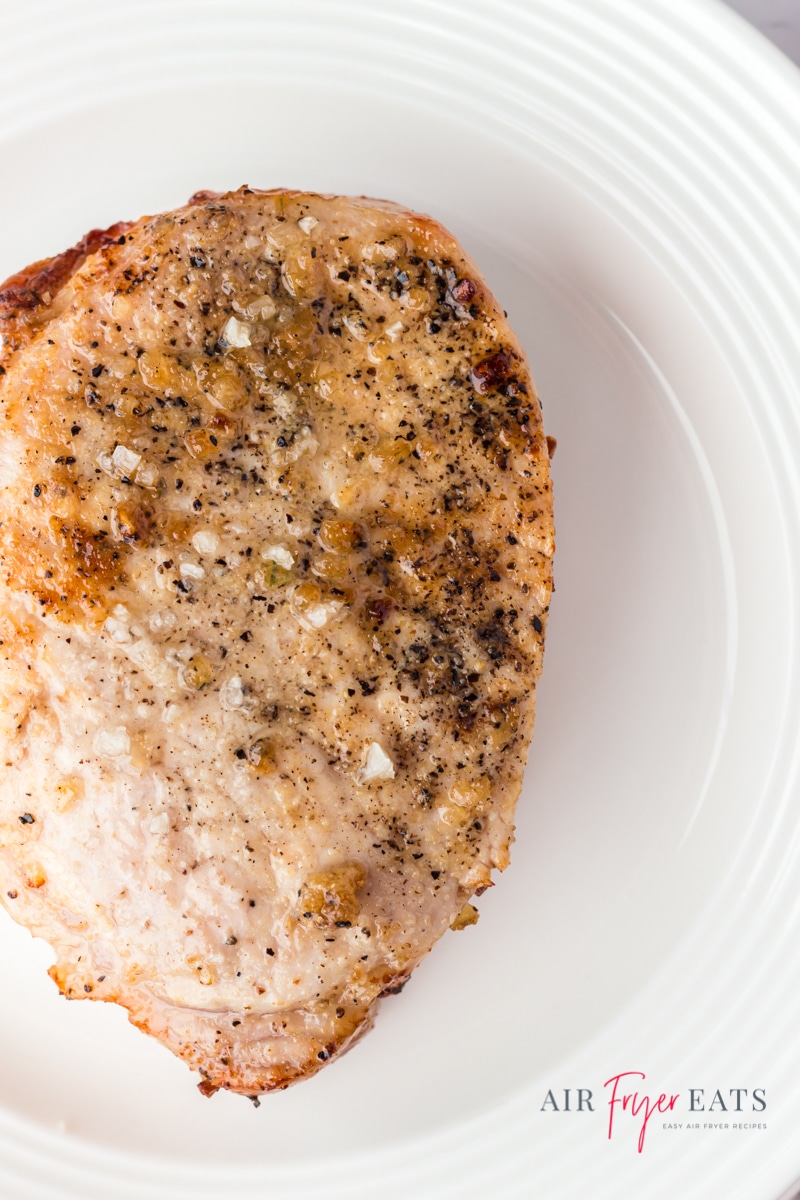 Closeup photo of a boneless pork chop on a white plate.