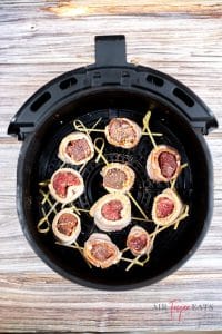 Black air fryer basket containing 10 bacon wrapped steak bites