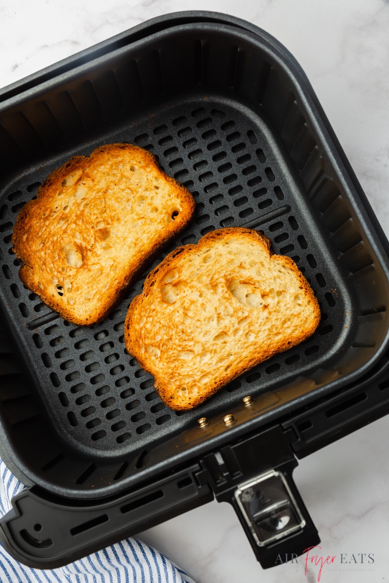a square cosori air fryer basket holding two slices of toasted bread