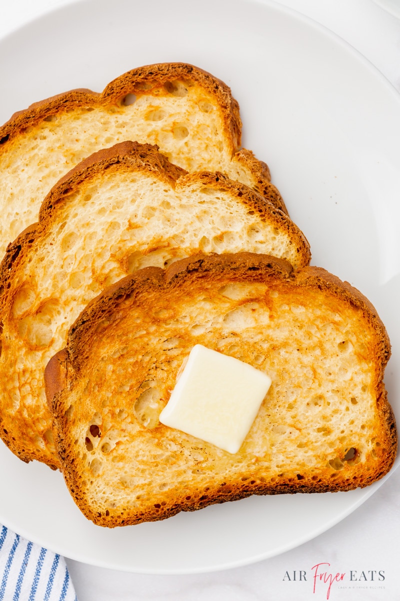 three pieces of air fryer white bread toast on a white plate. a pat of butter sits on top of one slice