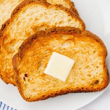 square crop of a plate of toasted white bread. a pat of butter sits on top of the top piece of toast