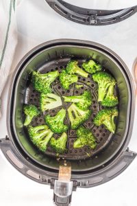 overhead shot of cooked broccoli in black air fryer basket on a white background