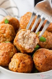 closeup shot of a bowl of cooked meatballs, a fork is holding one with a bite taken to show the internal texture