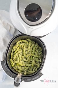 Photo of a white air fryer basket containing edamame ready to be cooked