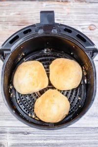 Black air fryer basket containing three egg and bacon stuffed biscuits