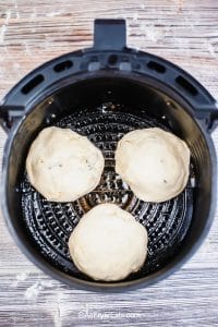 Black air fryer basket containing three air fryer egg and bacon stuffed biscuits