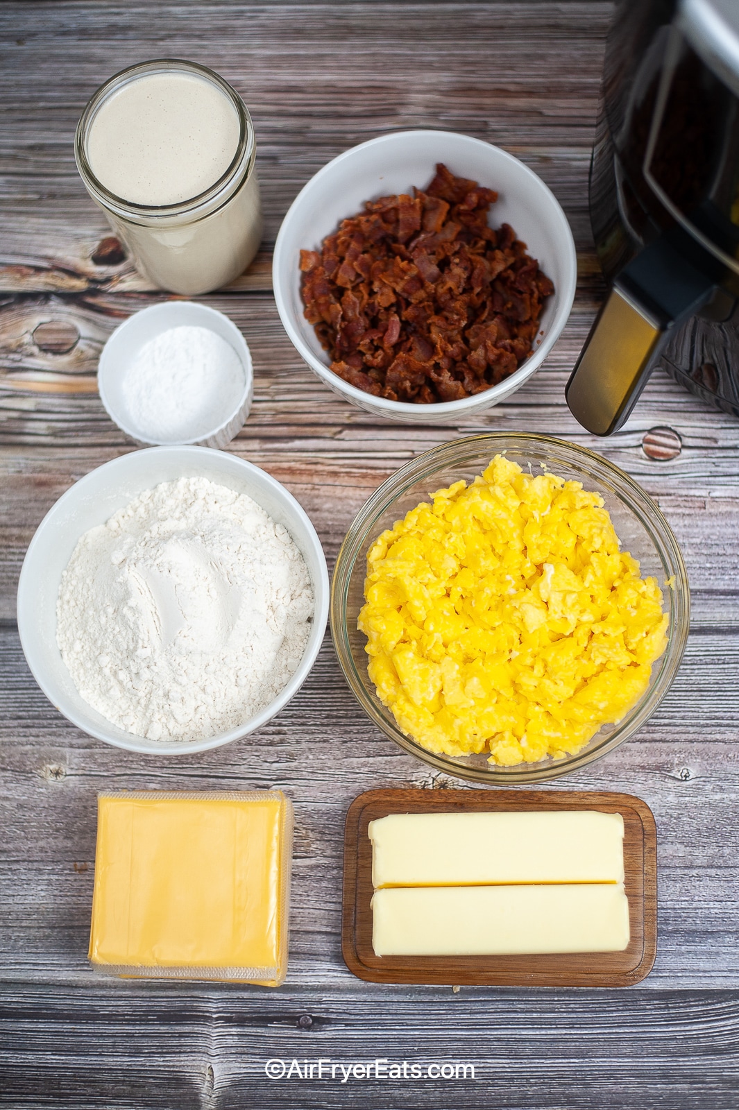 Overhead shot of ingredients required for air fryer egg and bacon stuffed biscuits: Flour, butter, milk, eggs, bacon and cheese