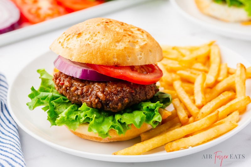 a deluxe beyond burger with lettuce tomato and onion on a plate with a side of french fries