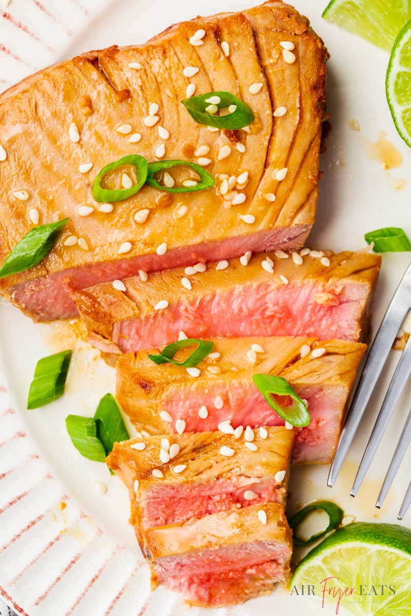 closeup view of an air fried ahi tuna steak topped with sesame seeds and green onion. The steak has been sliced to show the pink inside color and texture.