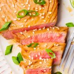 closeup view of an air fried ahi tuna steak topped with sesame seeds and green onion. The steak has been sliced to show the pink inside color and texture.