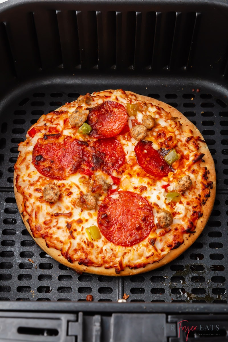 a personal sized pizza, cooked and in an air fryer basket. 