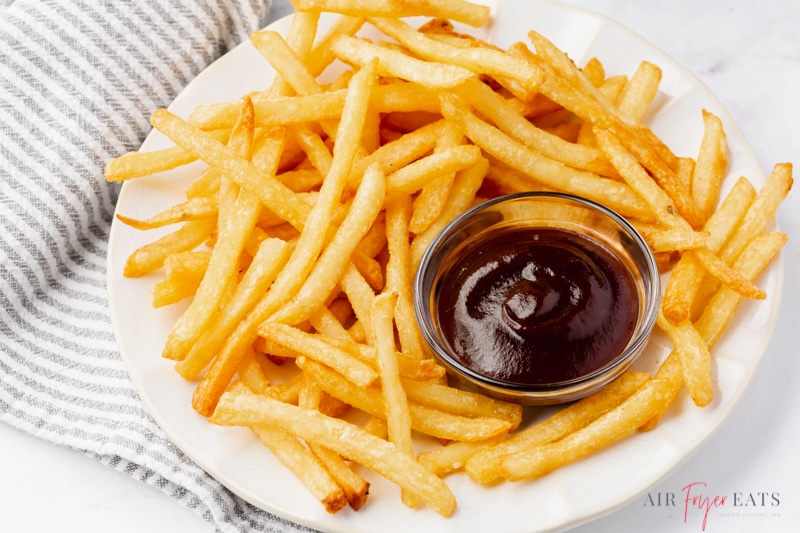 a plate of reheated french fries surrounding a cup of barbecue sauce