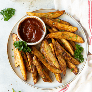 a plate of seasoned, cooked potato wedges with a side cup of ketchup.