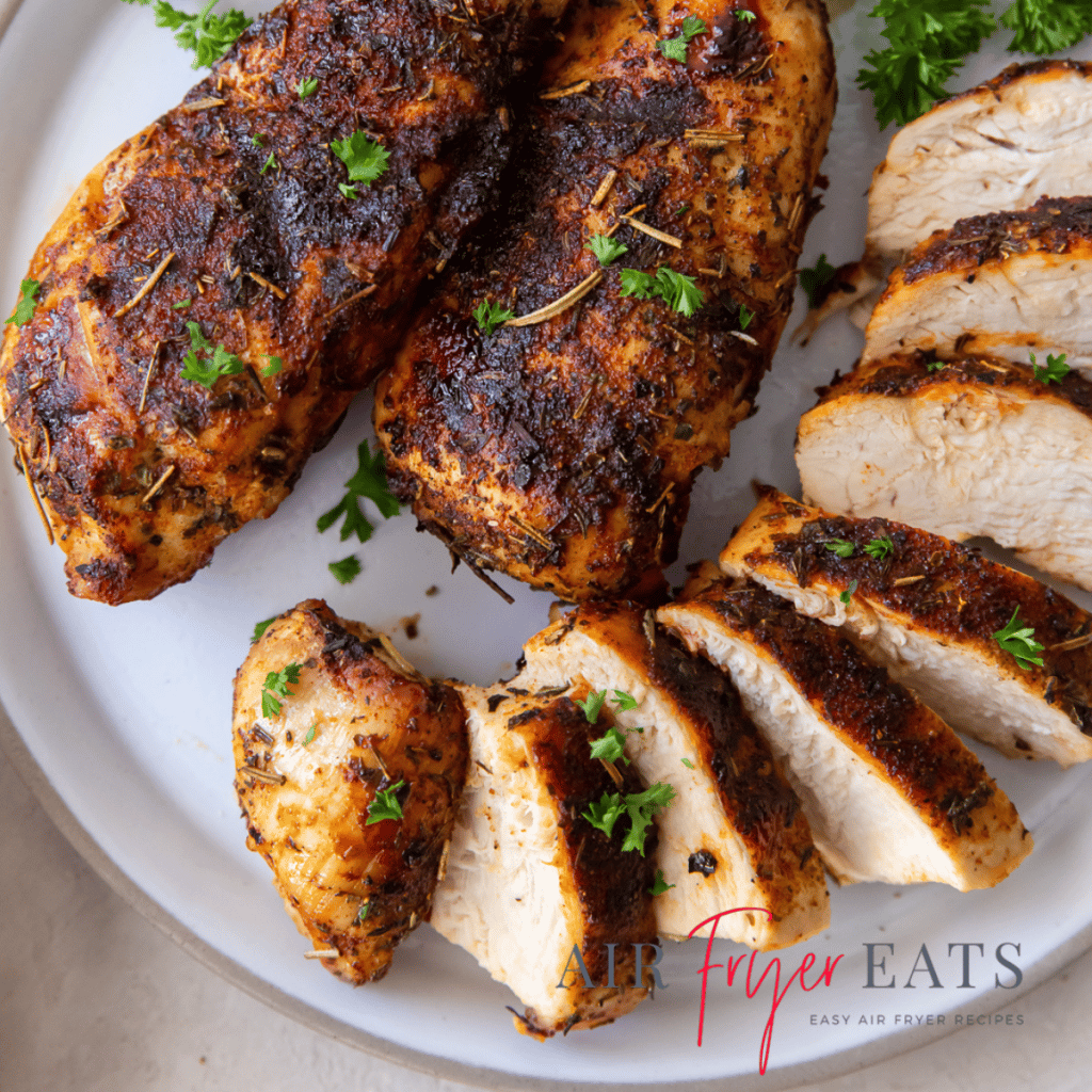 chicken breast sliced on a white plate with green herbs on top and to the side.