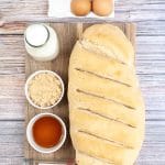 Vertical photo of ingredients required to make air fryer french toast. French bread loaf, milk, eggs and spices