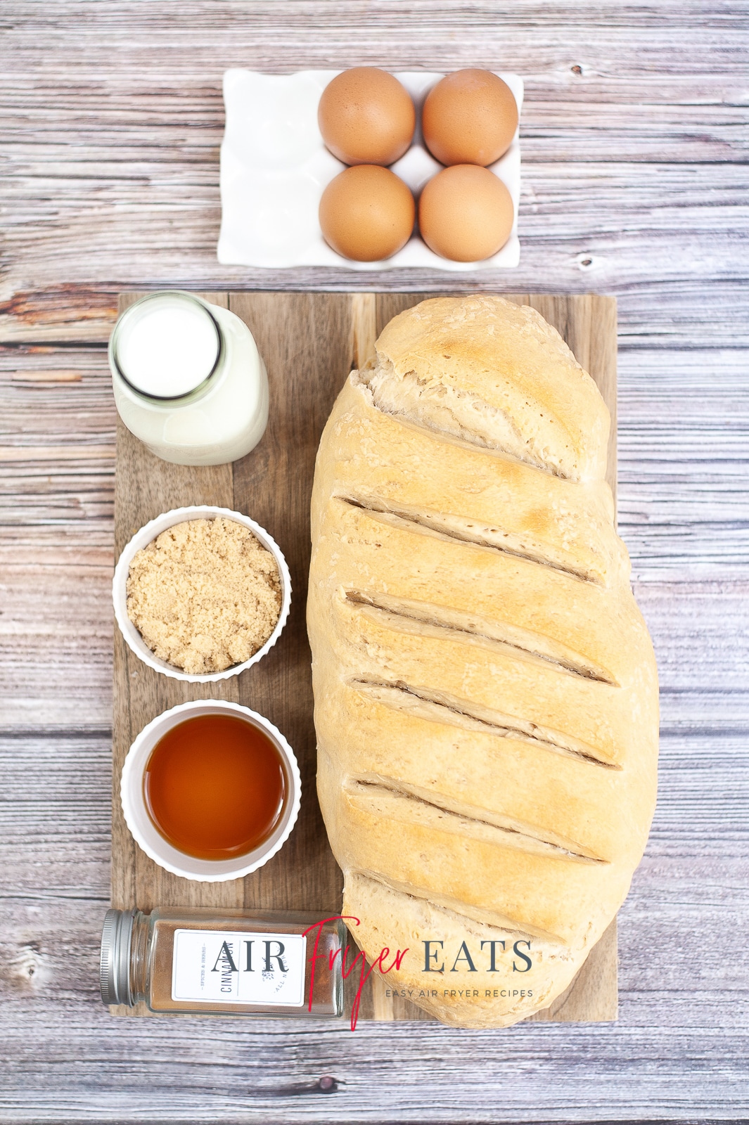 Vertical photo of ingredients required to make air fryer french toast. French bread loaf, milk, eggs and spices