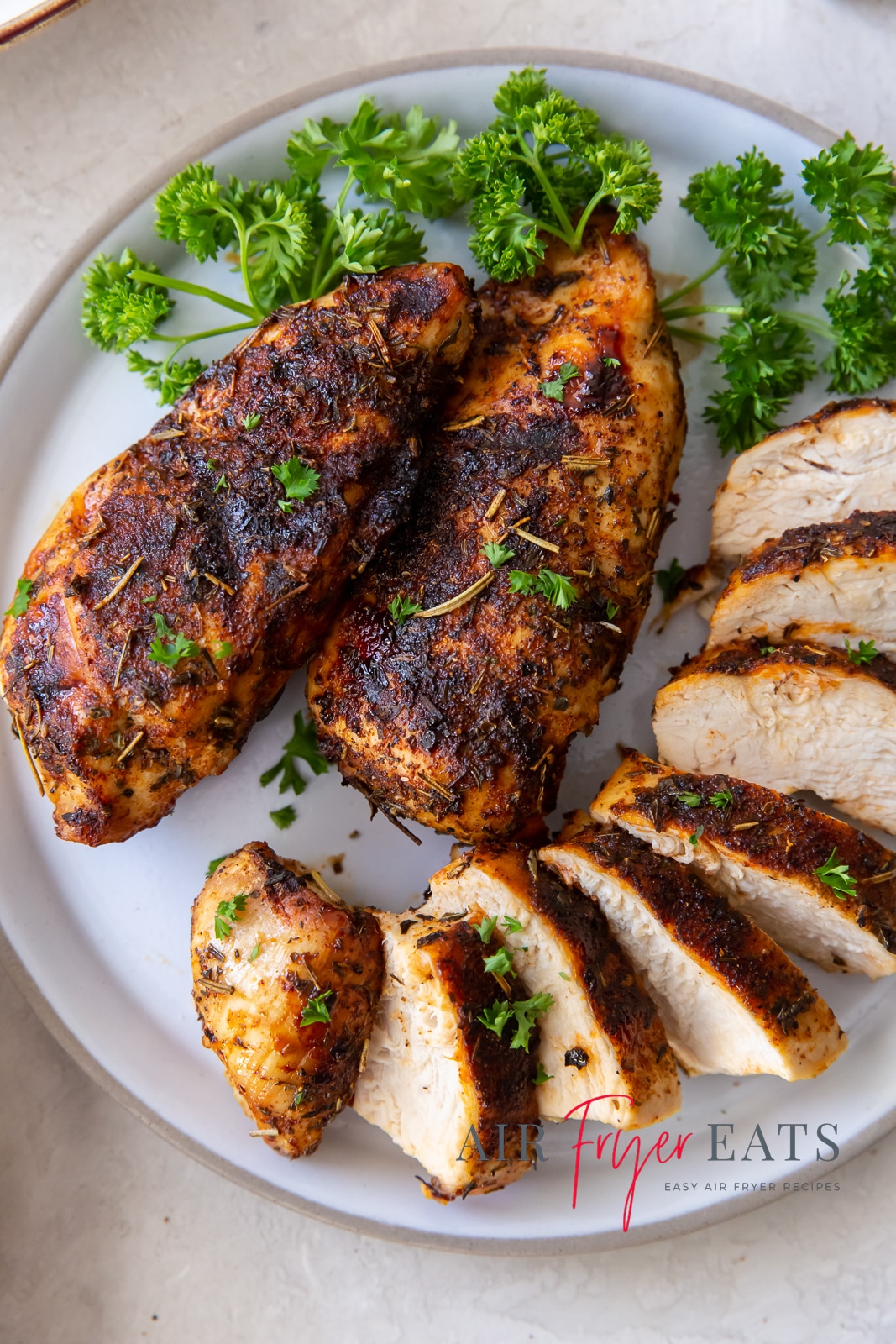 chicken breast sliced on a white plate with green herbs on top and to the side.