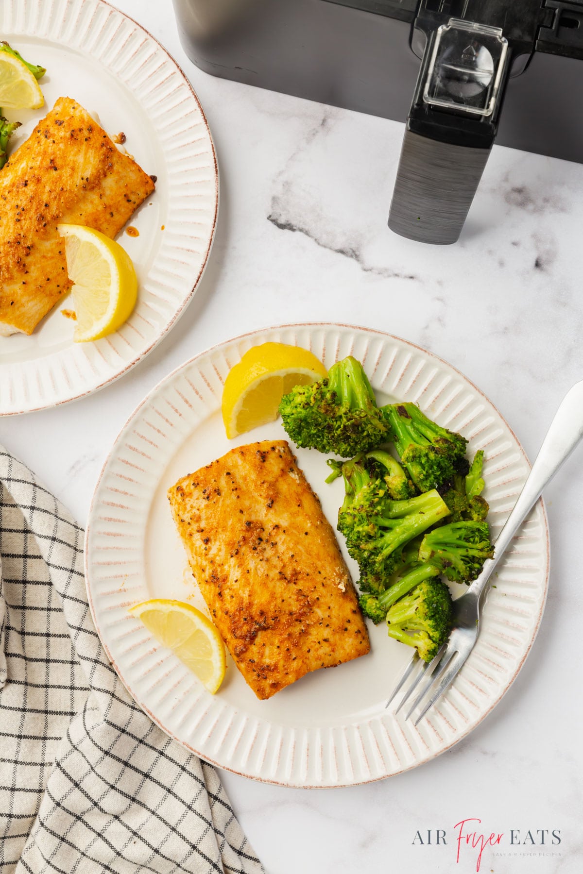 two dinner plates of mahi mahi and broccoli next to a cosori air fryer basket