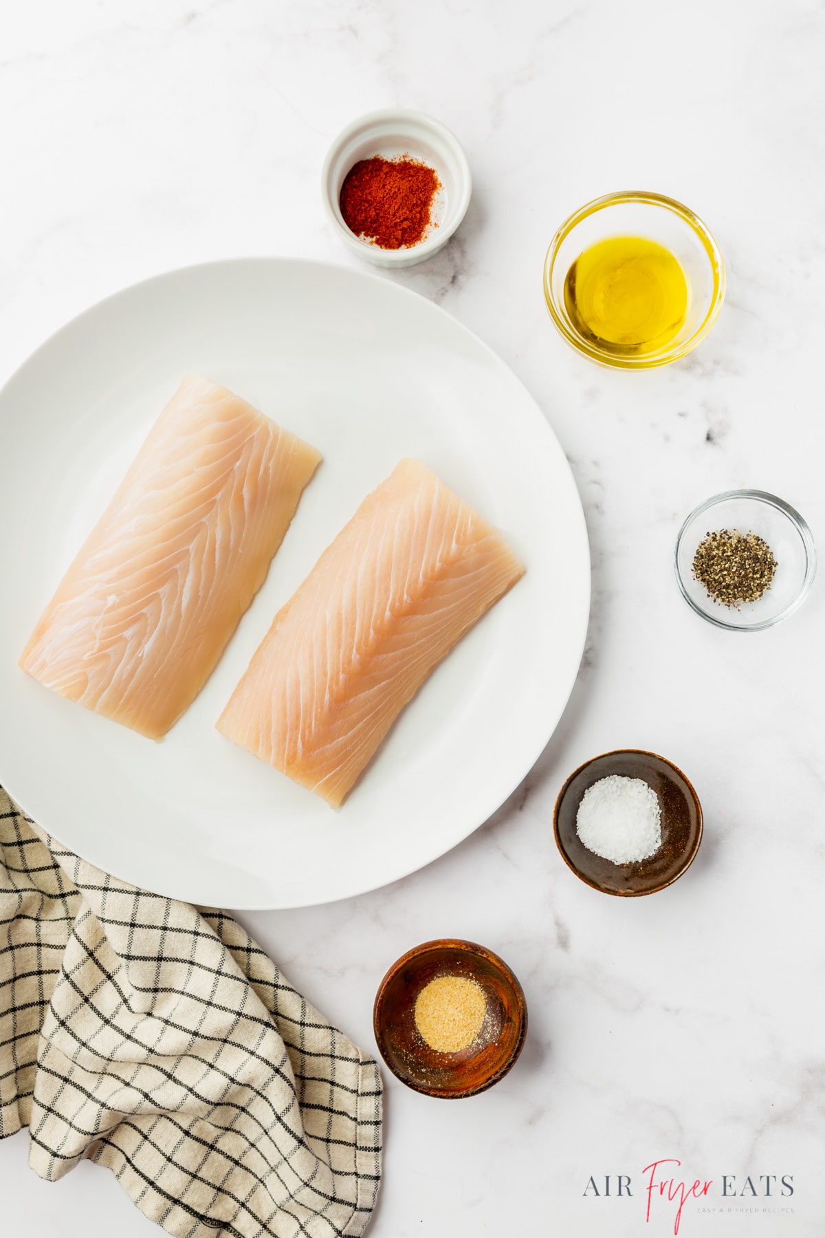 The ingredients needed to make air fryer mahi mahi, with a plate of two fillets next to small bowls of oil and seasoning.