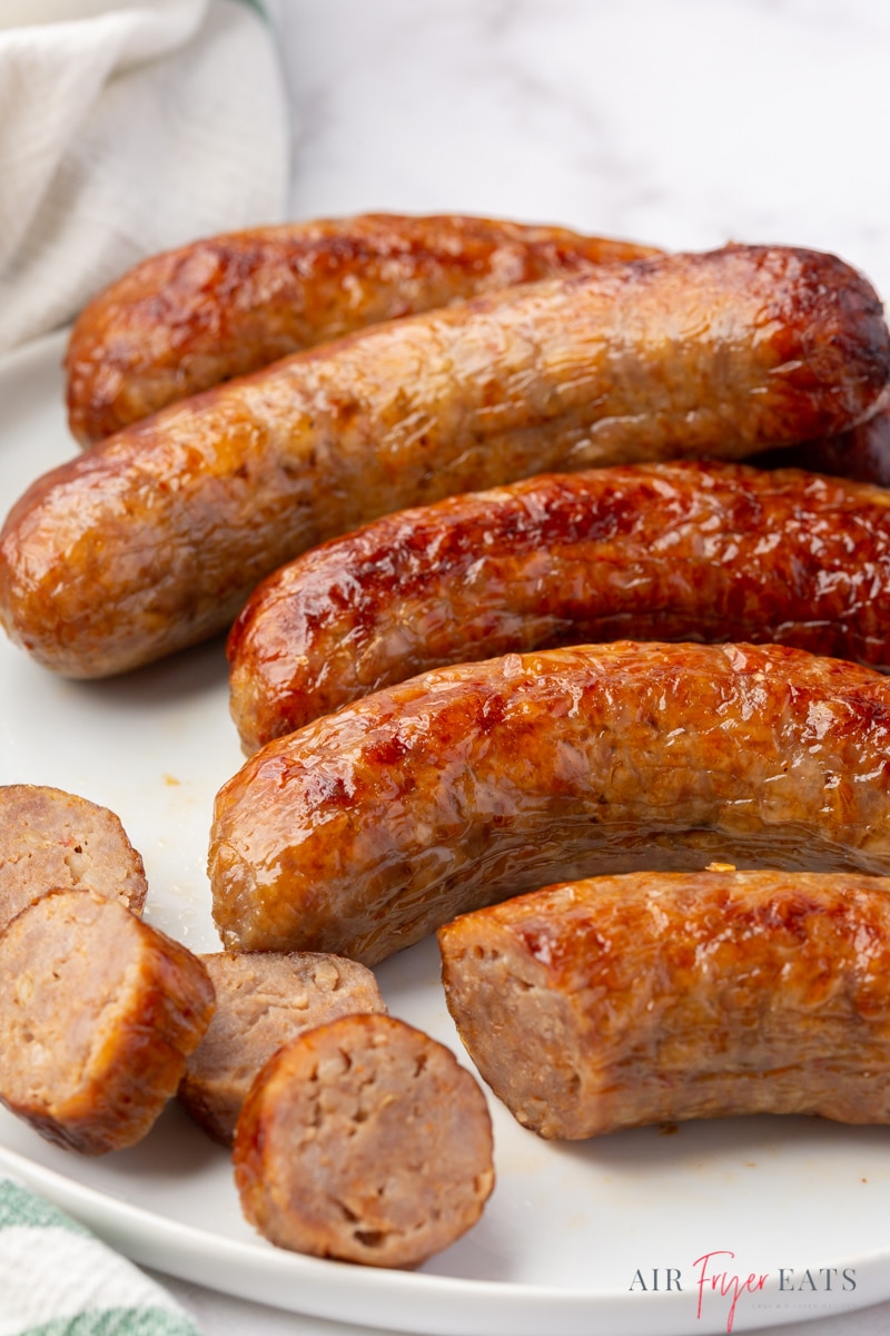 a plate of sausages. One has been sliced into bite sized pieces. 