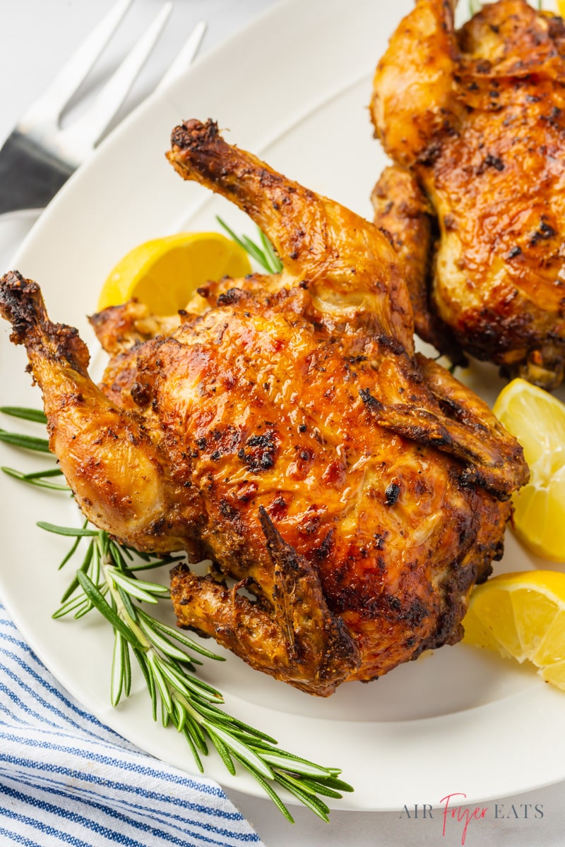 an air fryer cornish hen on a platter with lemons and fresh tyme