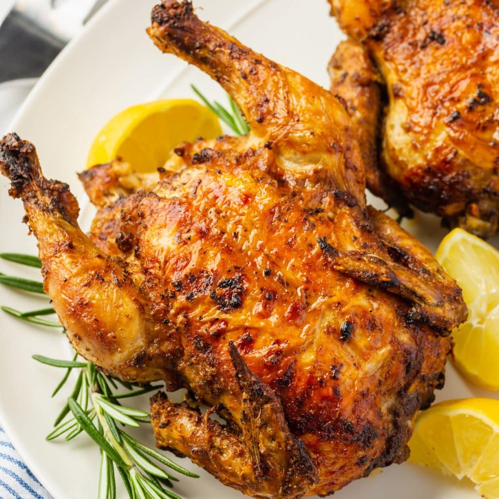 an air fryer cornish hen on a platter with lemons and fresh tyme