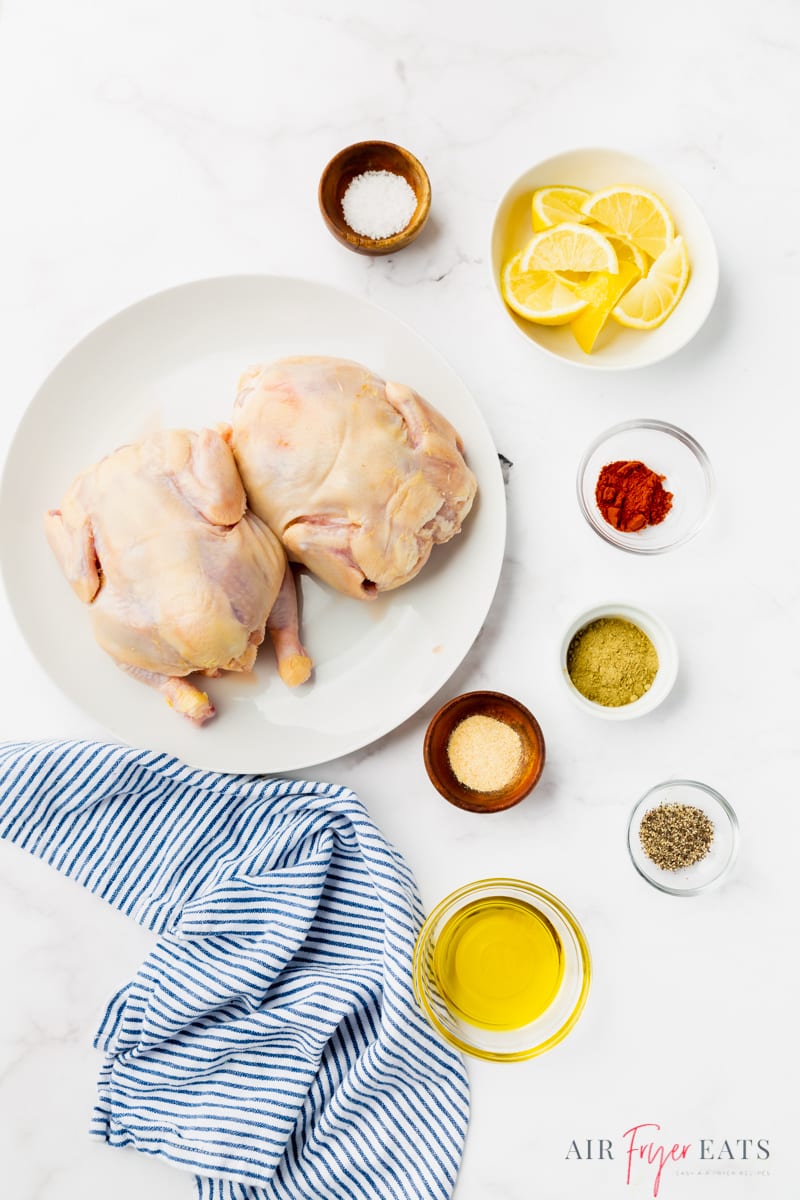 The ingredients needed to make air fryer cornish hen, including two birds, oil, lemons, and seasonings, measured into small bowls