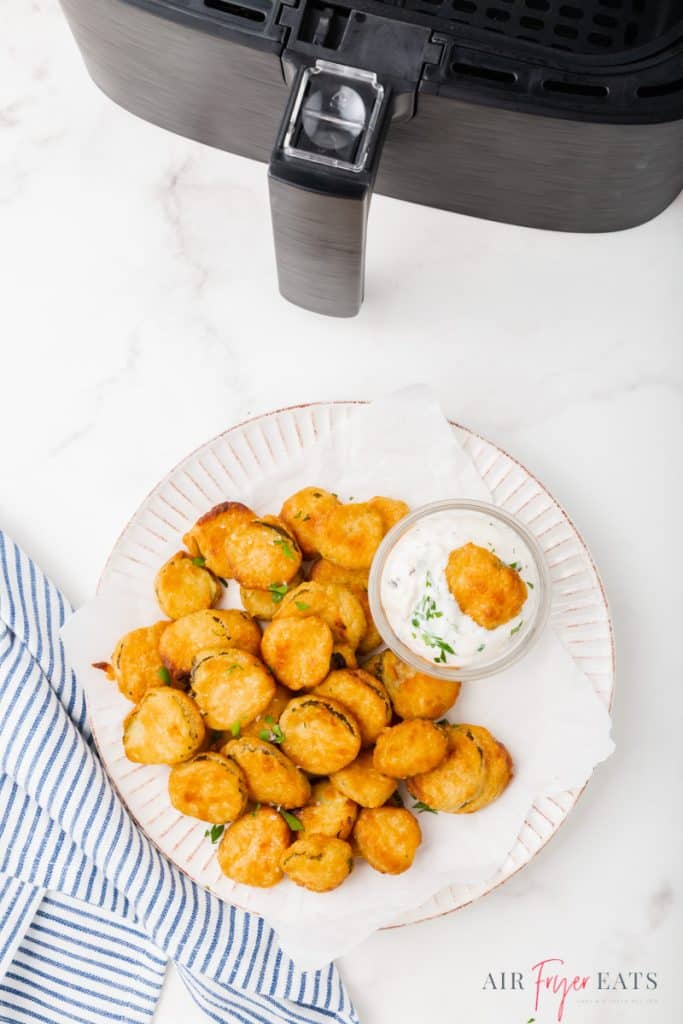 a plate of air fryer fried pickles and a side of ranch, next to an air fryer basket