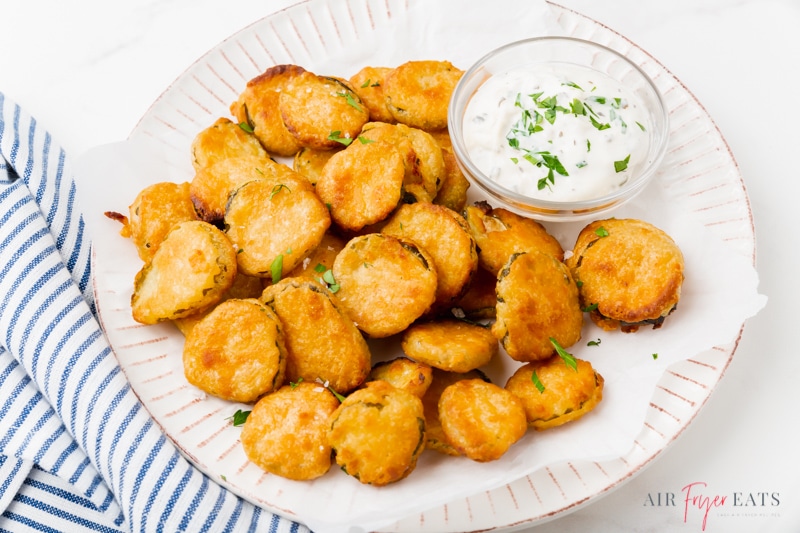 a white plate filled with fried pickles with a side of ranch.