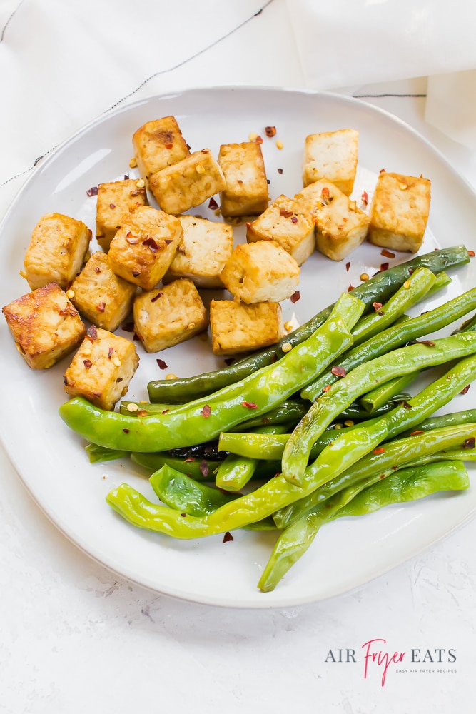 Vertical photo of a white plate containing air fried tofu cubes and green beans