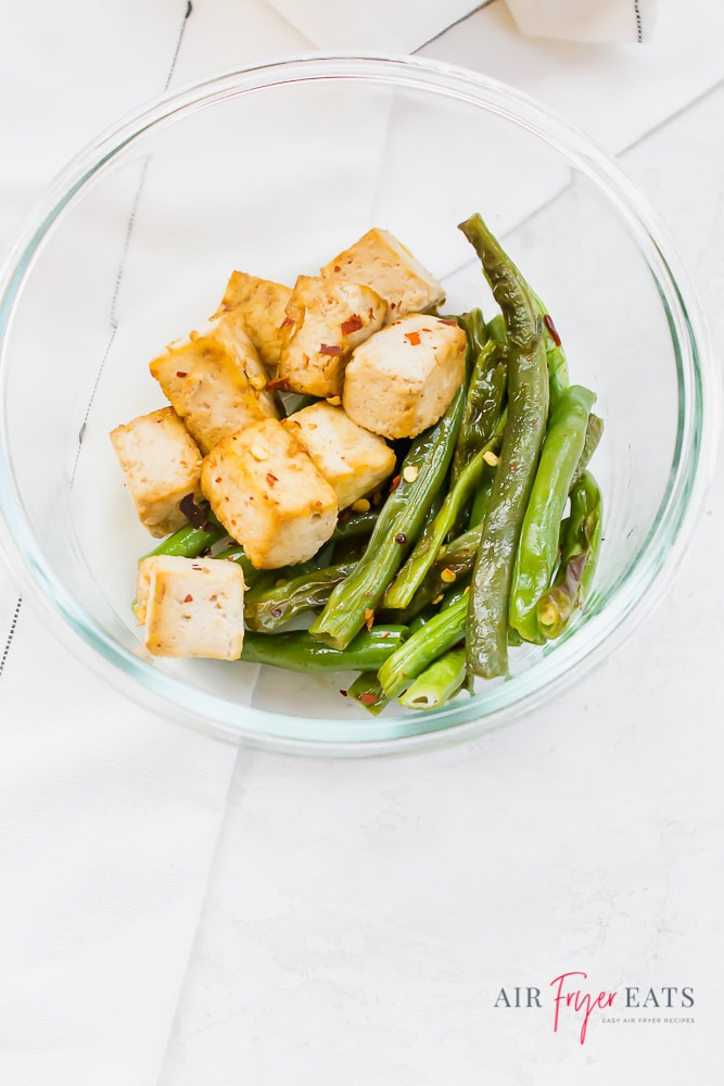 Vertical photo of a glass bowl containing air fried tofu cubes and green beans